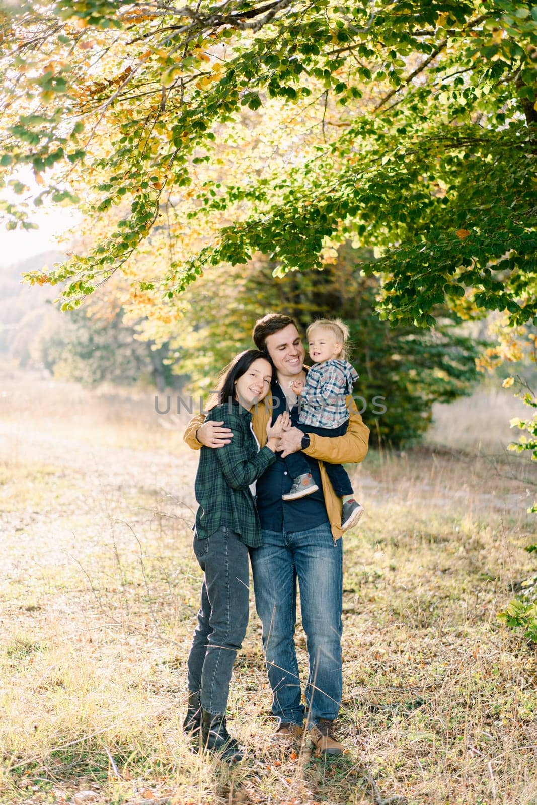 Mom hugs dad with a little girl in his arms while standing in the autumn forest. High quality photo