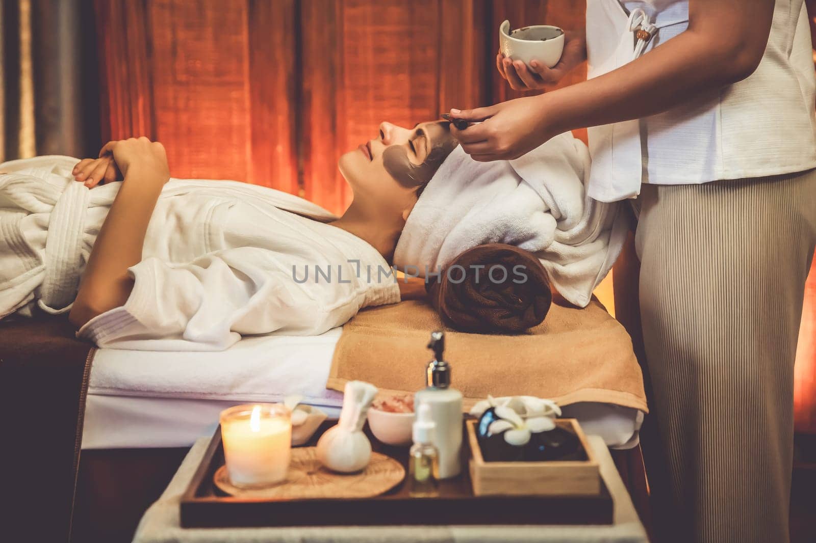 Spa salon composition set up table on blurred background of woman customer in rejuvenating by luxurious face cream massage with warm lighting candle. Facial skin treatment and beauty care. Quiescent