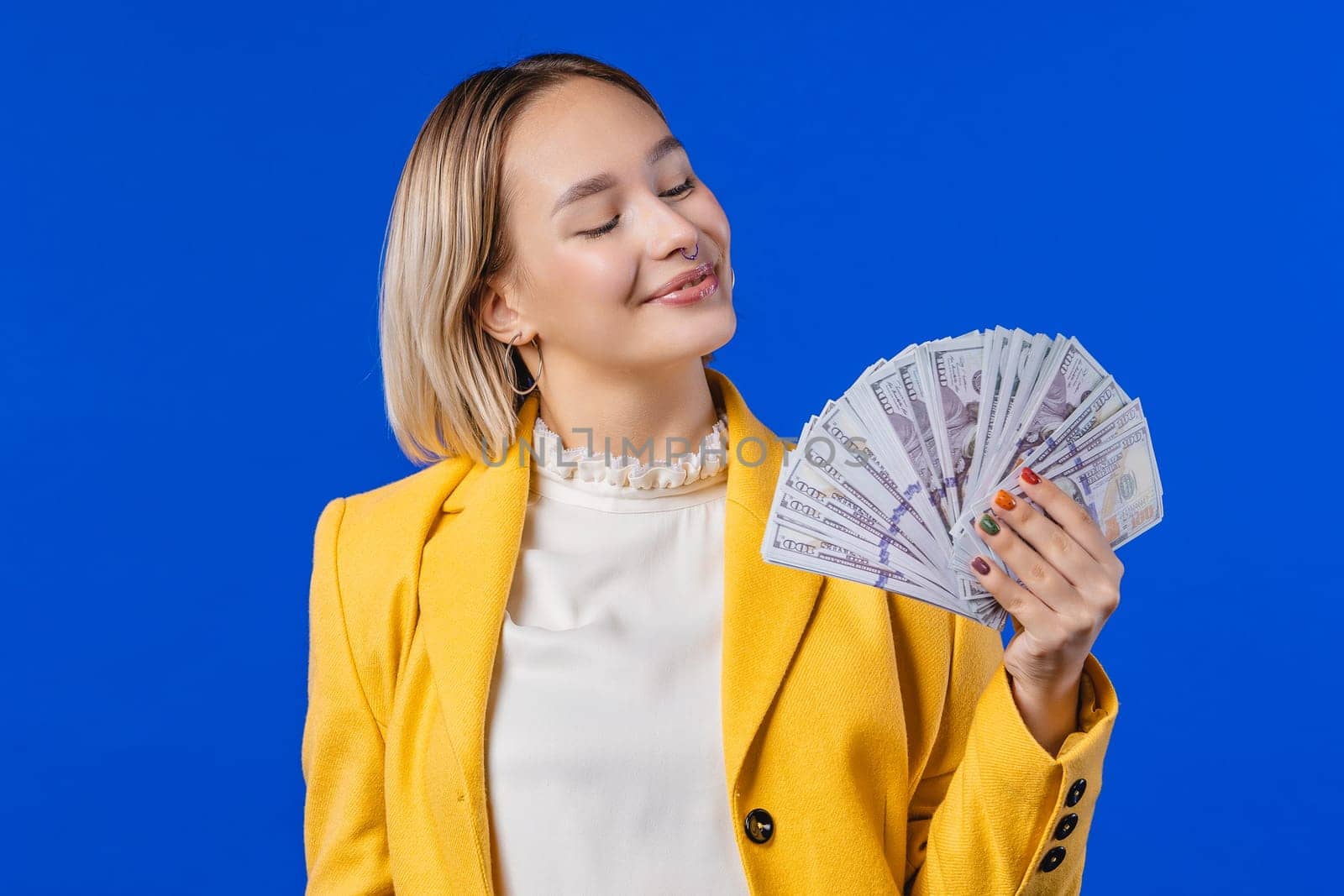 Rich excited blonde woman with cash money USD currency dollars banknotes on blue by kristina_kokhanova