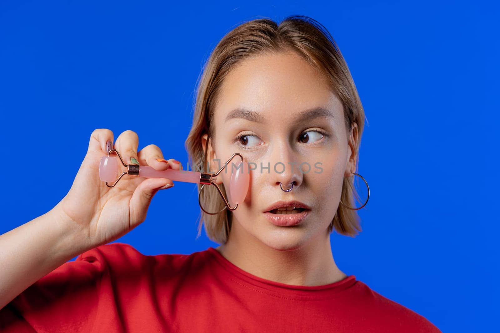 Teen girl with rose quartz stone roller on blue background. Facial self care, beauty rituals, cosmetology, anti aging and anti-wrinkle treatment. High quality photo