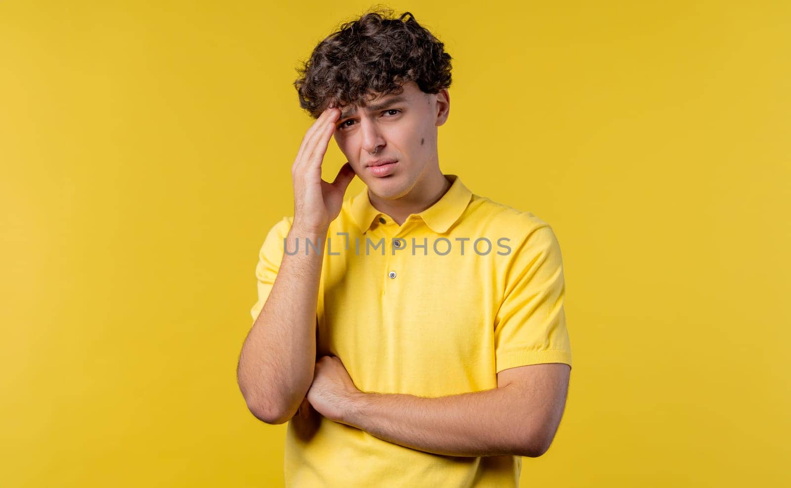 Young man having headache, studio portrait. Guy putting hands on head, isolated on yellow background. Concept of problems, medicine, illness
