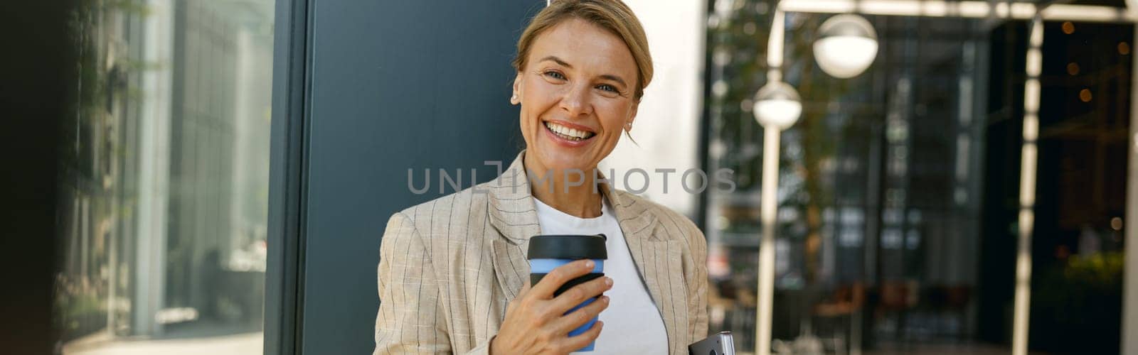 Positive female manager with laptop and take away coffee during break time in office
