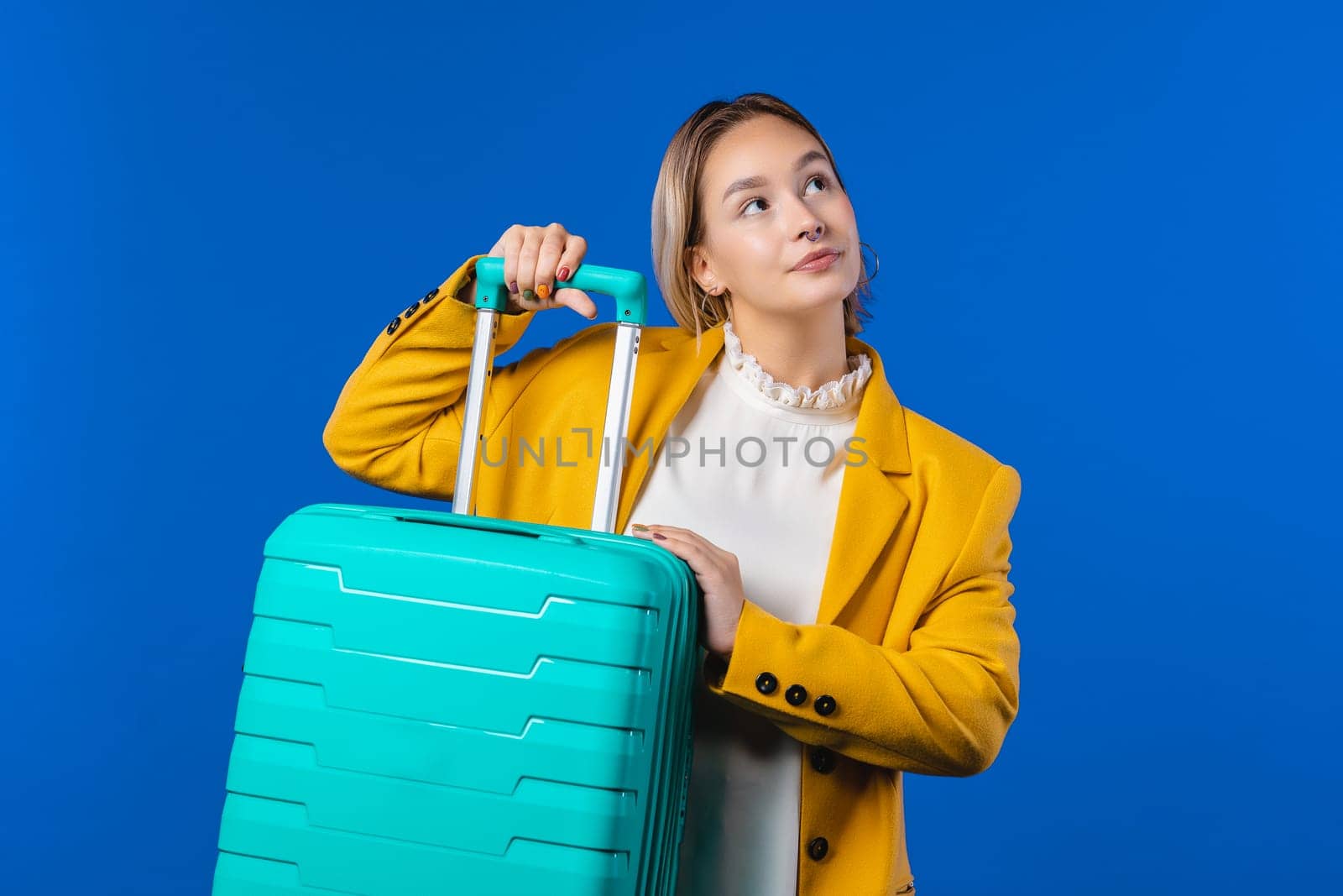 Young pretty woman with carry-on suitcase on blue. Luggage bag for airplane by kristina_kokhanova