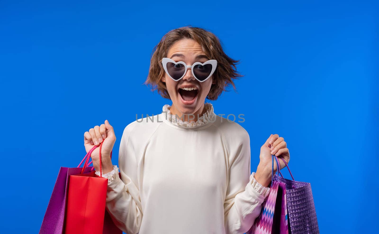 Excited woman with colorful paper bags after shopping on blue studio background by kristina_kokhanova