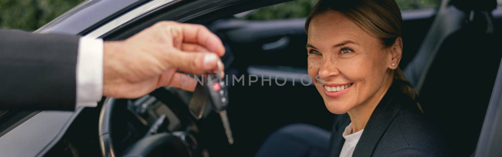 Smiling businesswoman receiving keys of her new status car from dealer. High quality photo