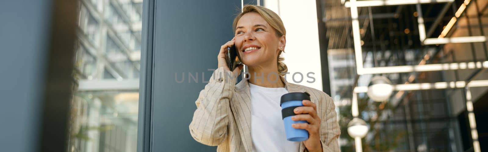 Smiling business woman talking phone while standing on building background and looks away