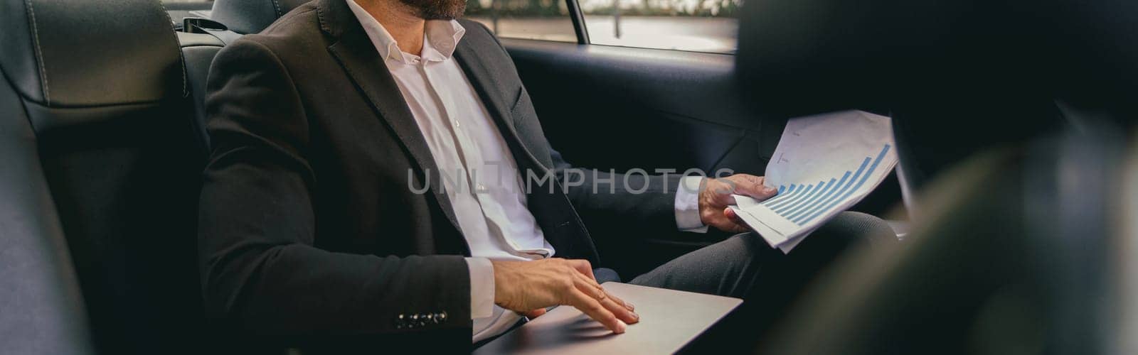 Male entrepreneur sitting on car backseat and working with documents while going to office by Yaroslav_astakhov