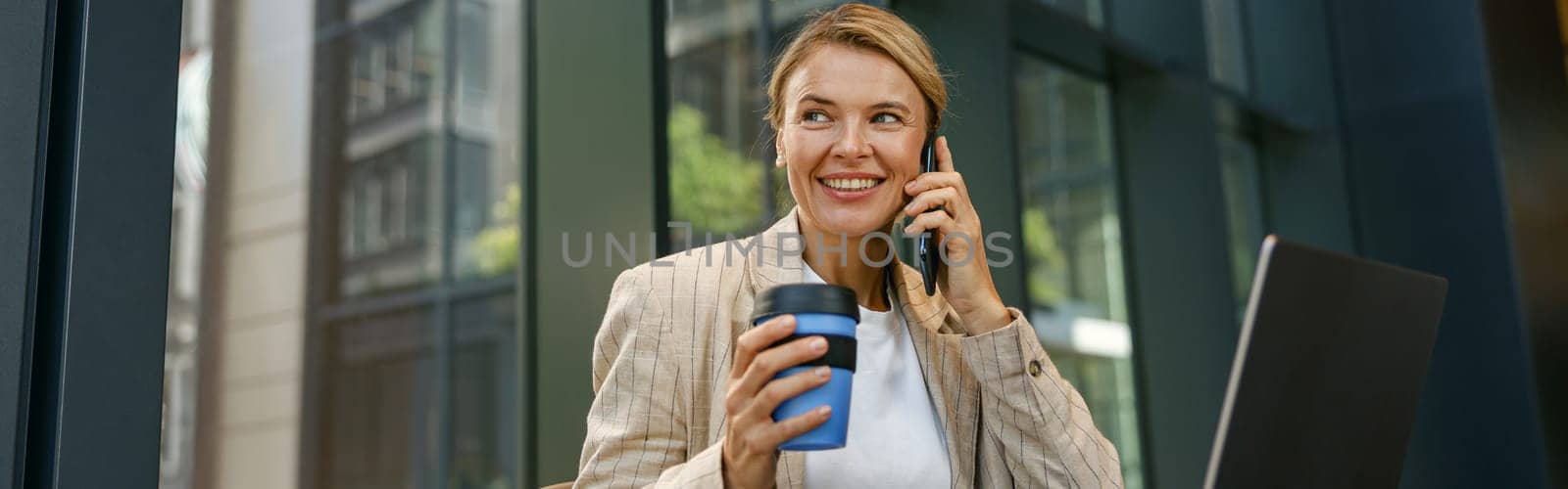Mature businesswoman talking on phone with client while working on laptop in office by Yaroslav_astakhov