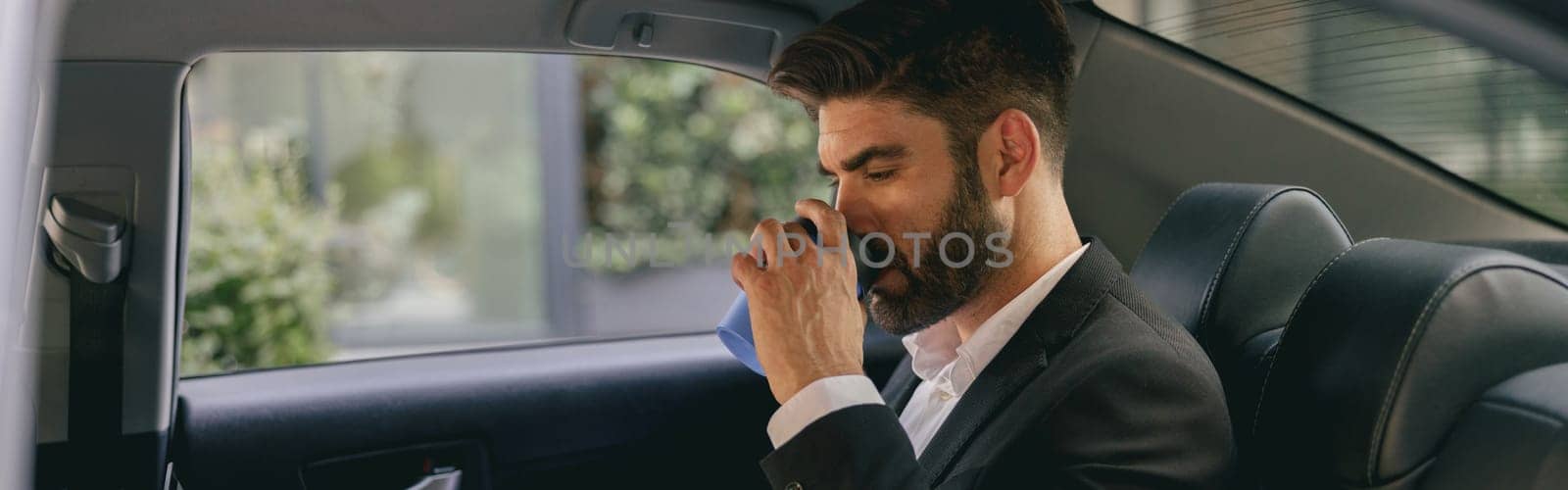 Professional male finansist working on laptop sitting car backseat and drinking coffee by Yaroslav_astakhov
