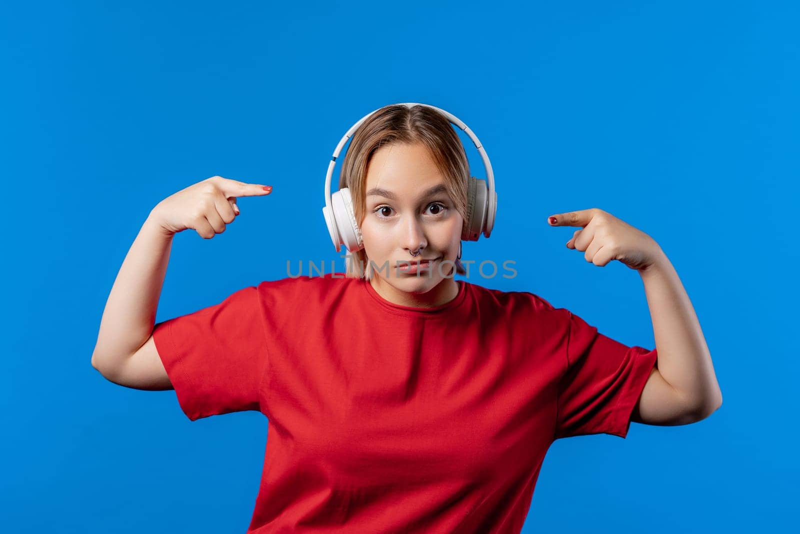 Positive woman listening music, enjoying with headphones on blue studio background. Radio, wireless modern sound technology, online player. High quality 4k