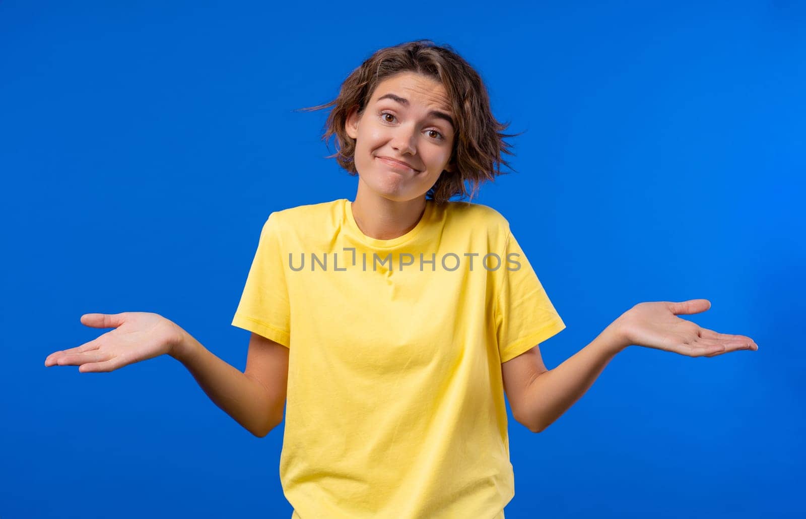 Confused pretty woman, shoulders up - can't help, makes gesture of I dont know. Difficult question, guilty reaction, puzzled stylish woman on blue background. High quality