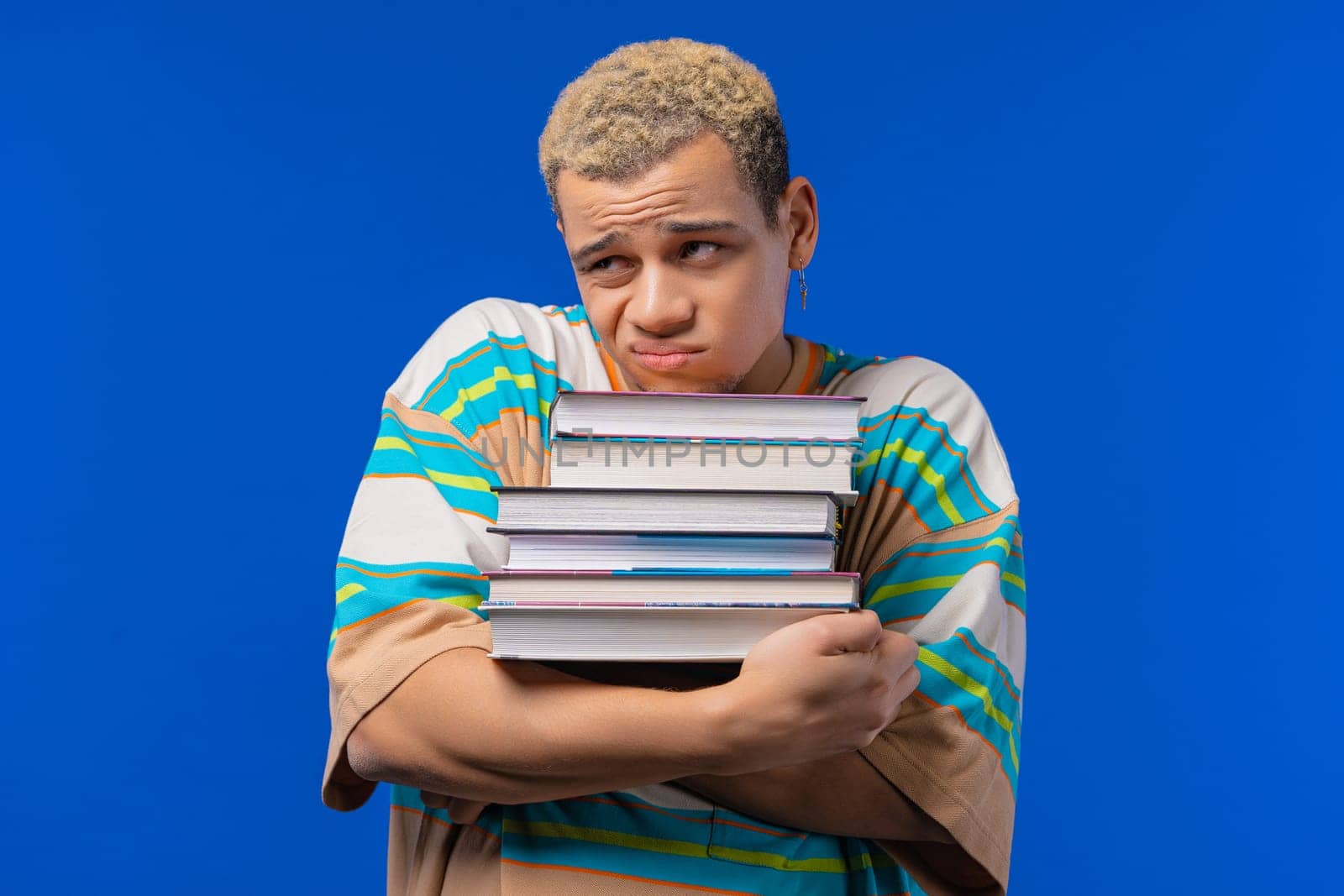 Lazy man student is dissatisfied with amount of books, homework in high school, blue background. Guy in displeasure, he is annoyed, discouraged frustrated by studies. High quality photo