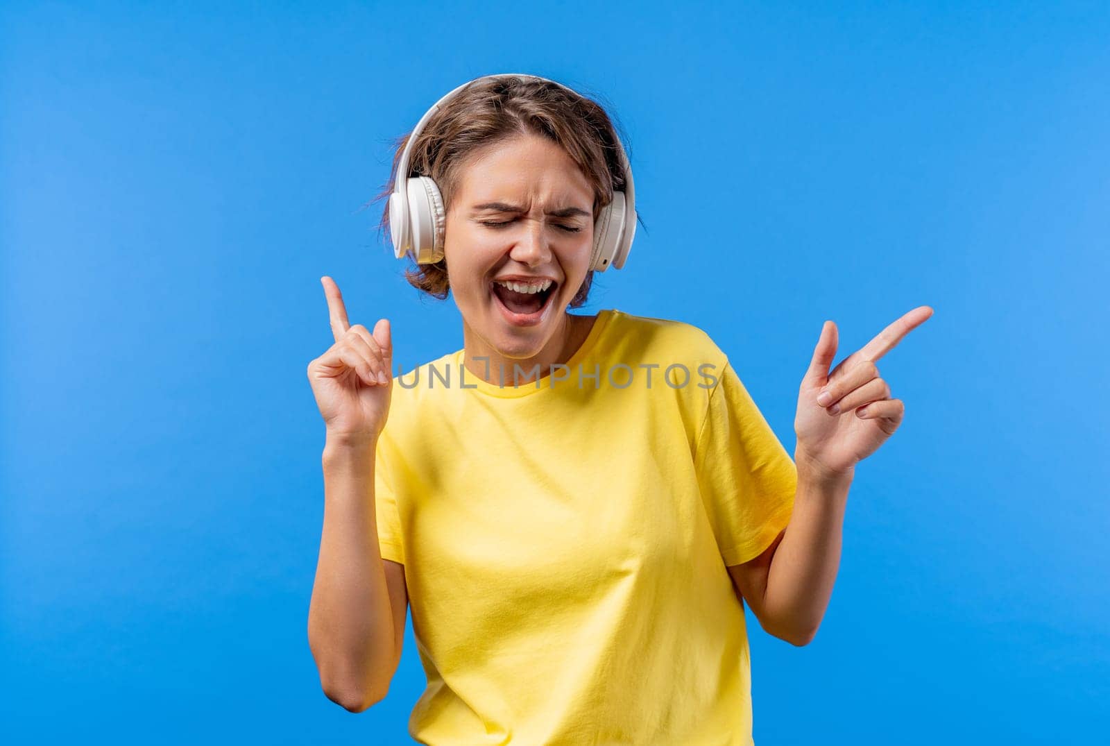 Positive woman listening music, enjoying with headphones, blue studio background by kristina_kokhanova