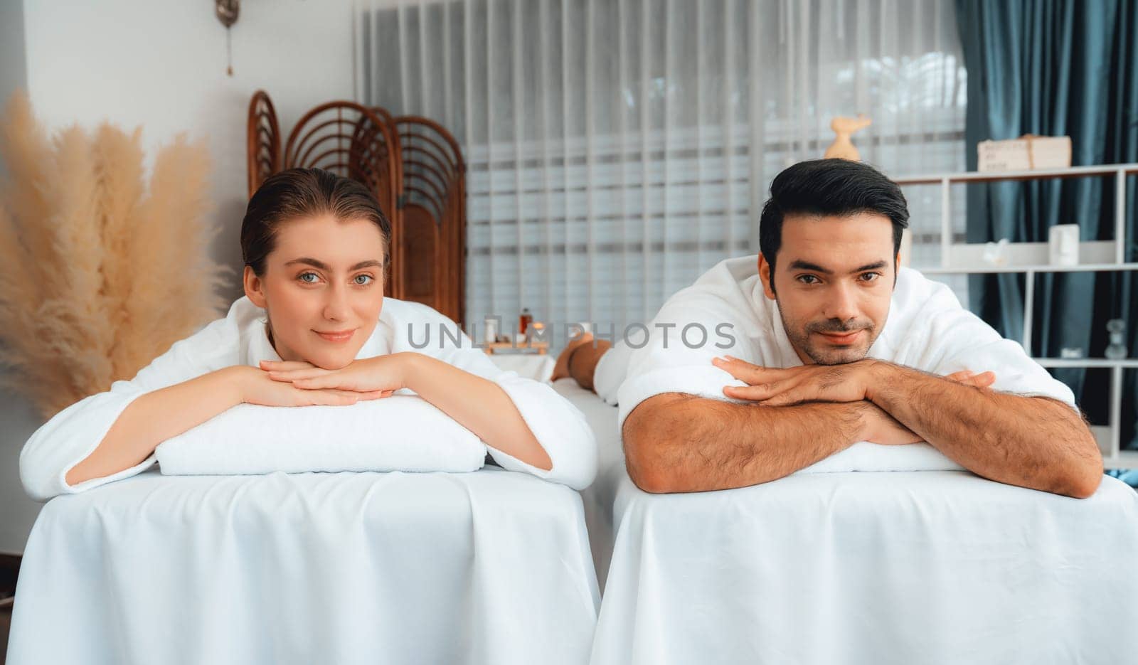 Caucasian couple customer enjoying relaxing anti-stress spa massage and pampering with beauty skin recreation leisure in day light ambient salon spa at luxury resort or hotel. Quiescent