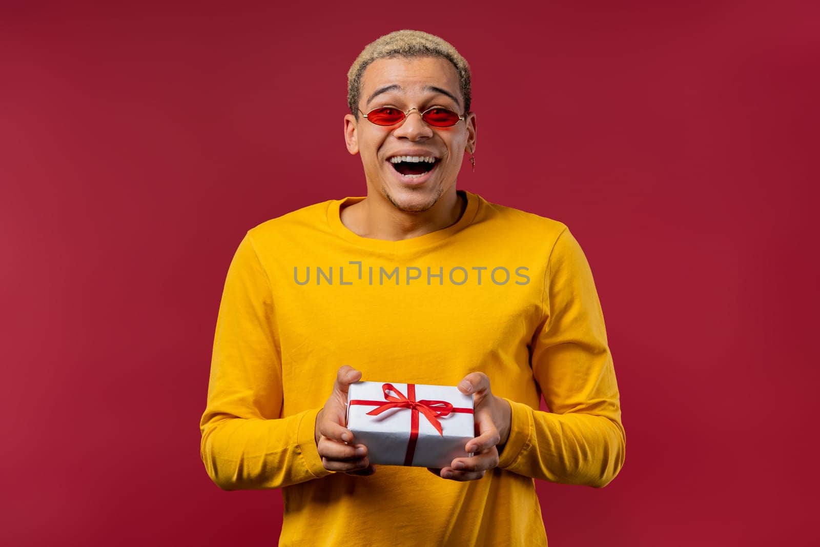 Handsome stylish man with gift box on red background. Guy smiling, he is happy with present. Offer, surprise for you. High quality photo