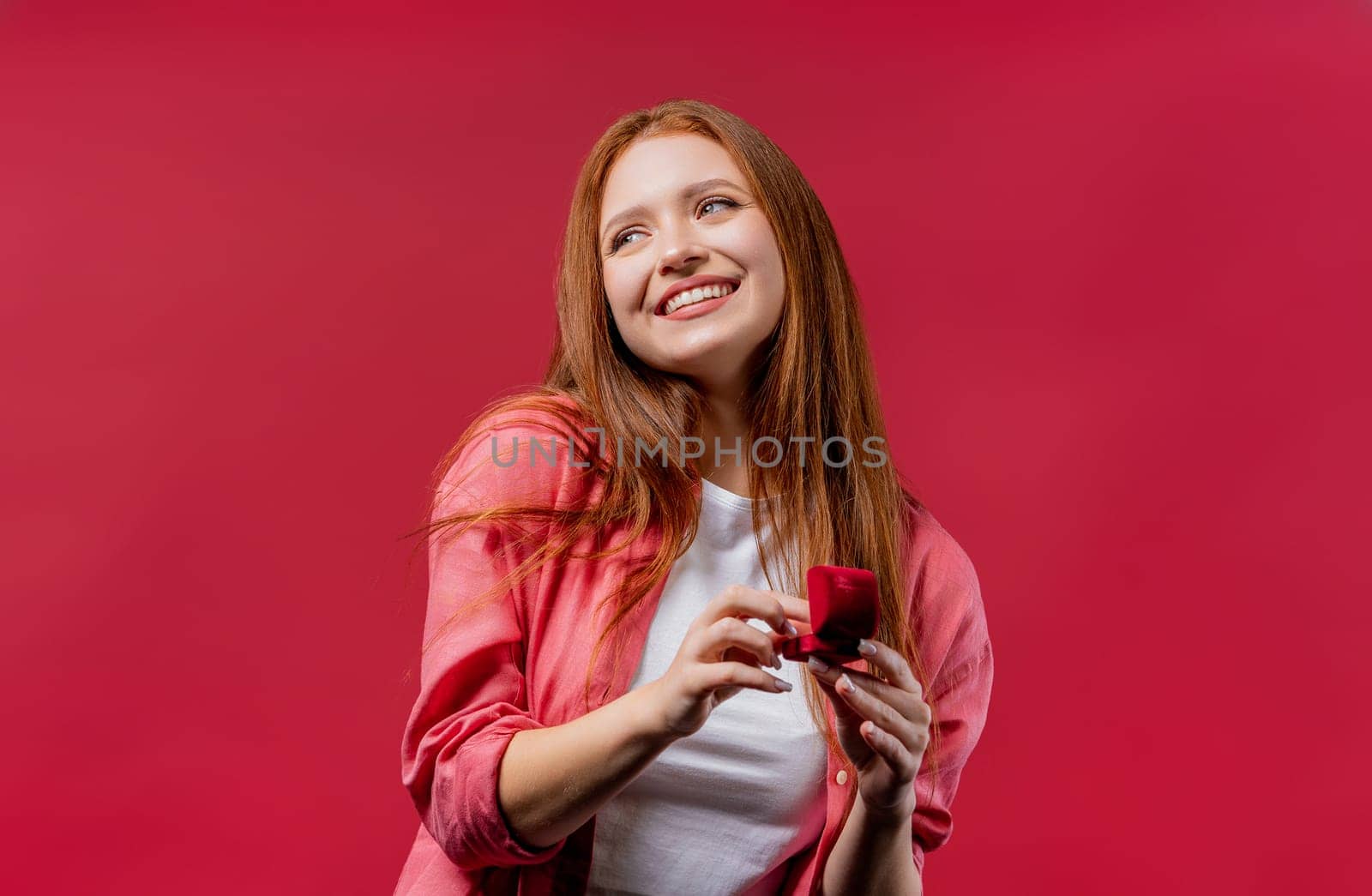 Pretty woman got jewelry box with proposal diamond ring on pink wall background. Surprised lady smiling, she is happy to be fiancee, proposition for marriage, st Valentines gift. High quality photo