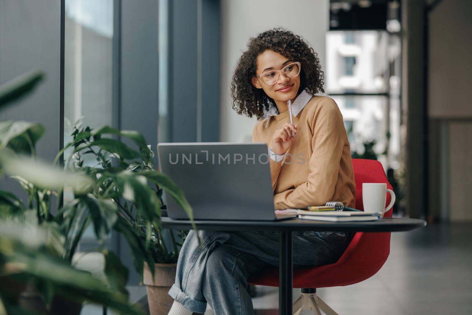 Pretty female manager in eyeglasses working on laptop while sitting in modern office near window