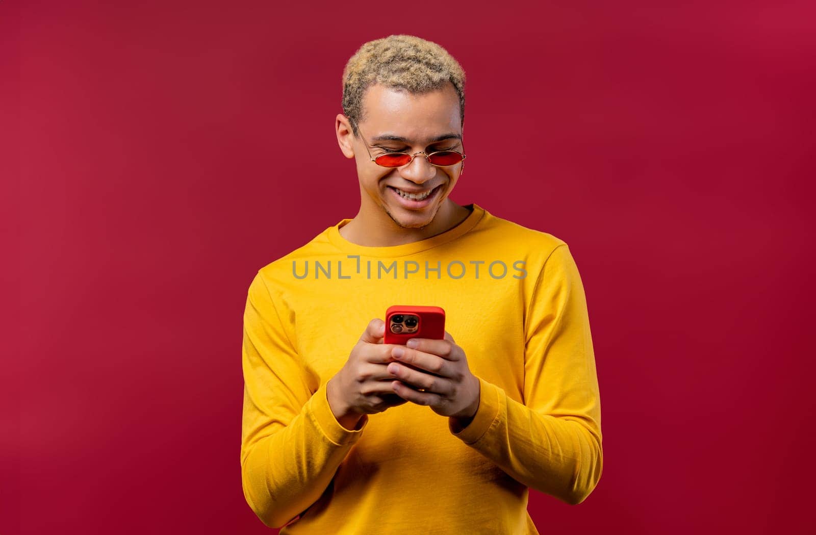 Handsome male teenager surfing internet on smartphone. Man with smile and joy on red background. Tech, success, happiness, social networks concept. High quality photo