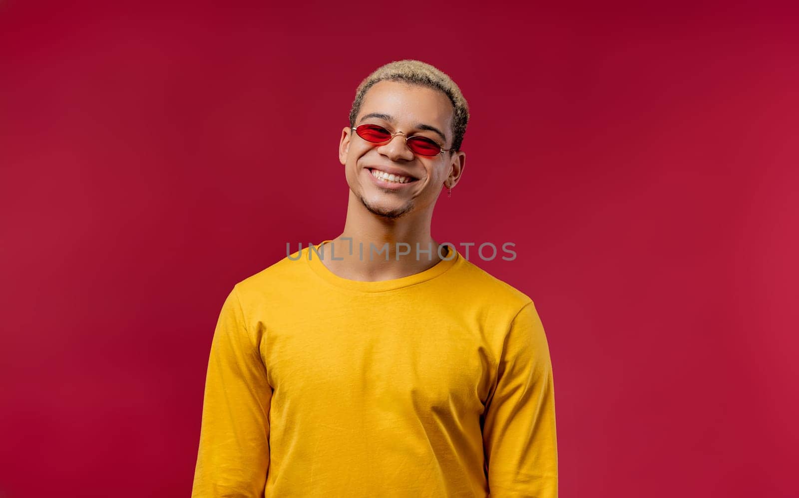 Handsome stylish man with trendy hairdo in yellow on red studio background. Cheerful guy smiling and looking to camera.