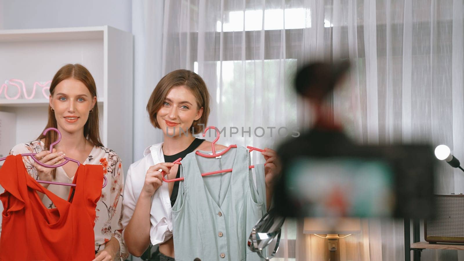 Two women influencer shoot live streaming vlog video review clothes prim social media or blog. Happy young girl with apparel studio lighting for marketing recording session broadcasting online.