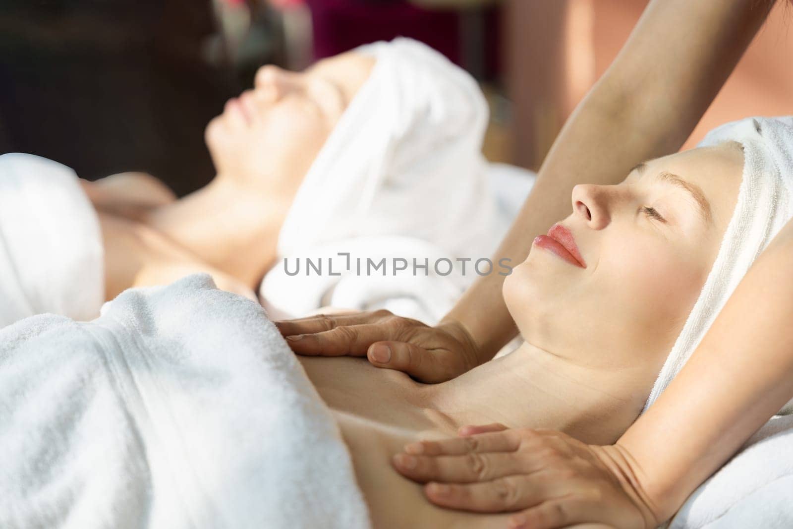 A portrait of two beautiful woman having back massage by professional masseur and falling in deep relaxation surrounded by traditional spa environment. Calming and relaxing concept. Tranquility.
