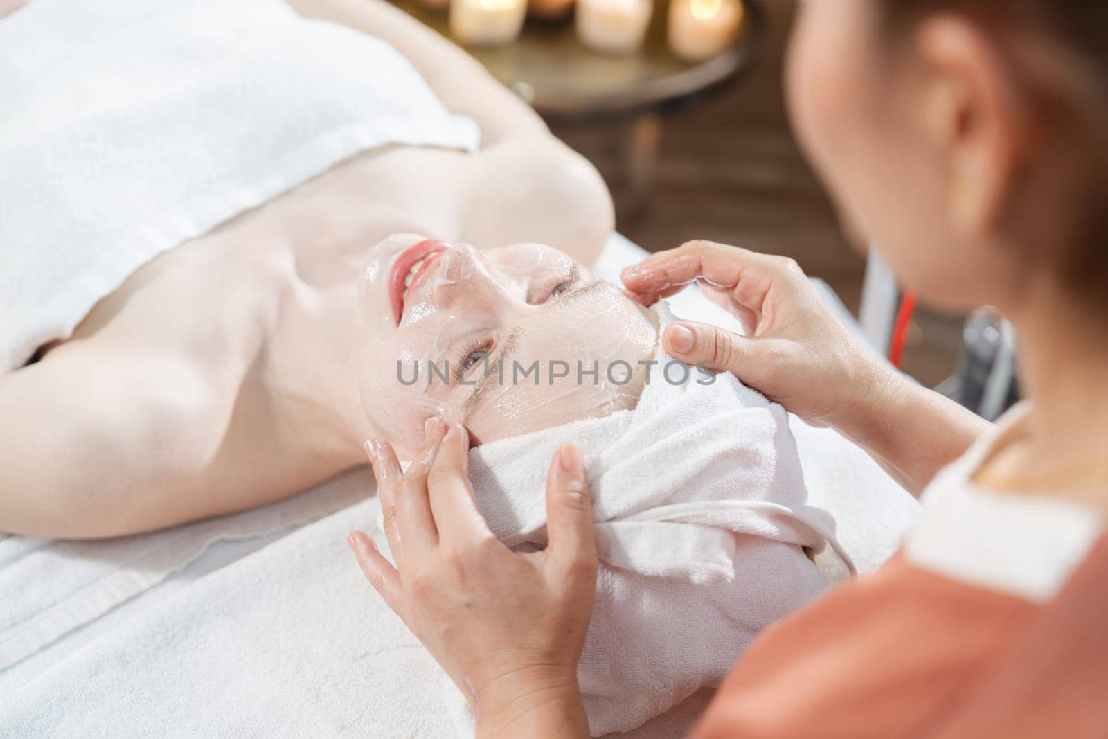 Portrait of beautiful caucasian woman having facial massage with homemade facial mask while lies on spa bed surrounded by beauty electrical equipment and peaceful nature environment. Tranquility.