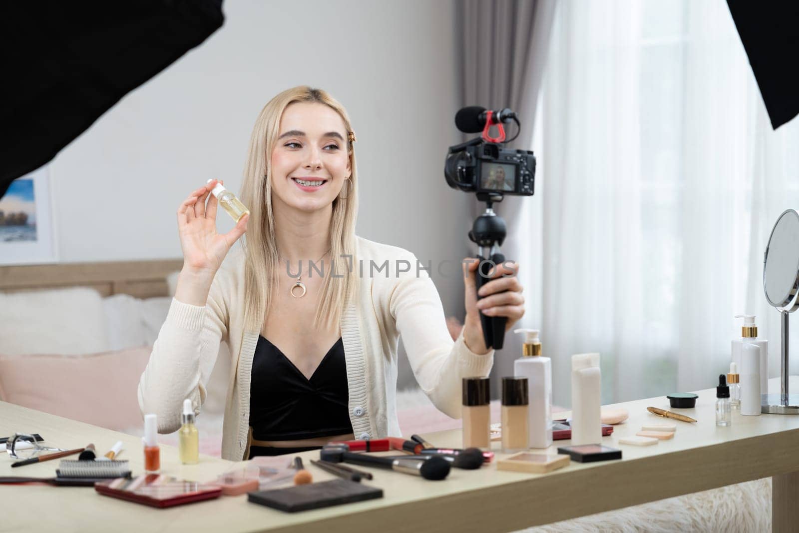 Young woman making beauty and cosmetic tutorial video content for social media. Beauty blogger smiles to camera while showing how to apply beauty skincare to audience or followers. Blithe