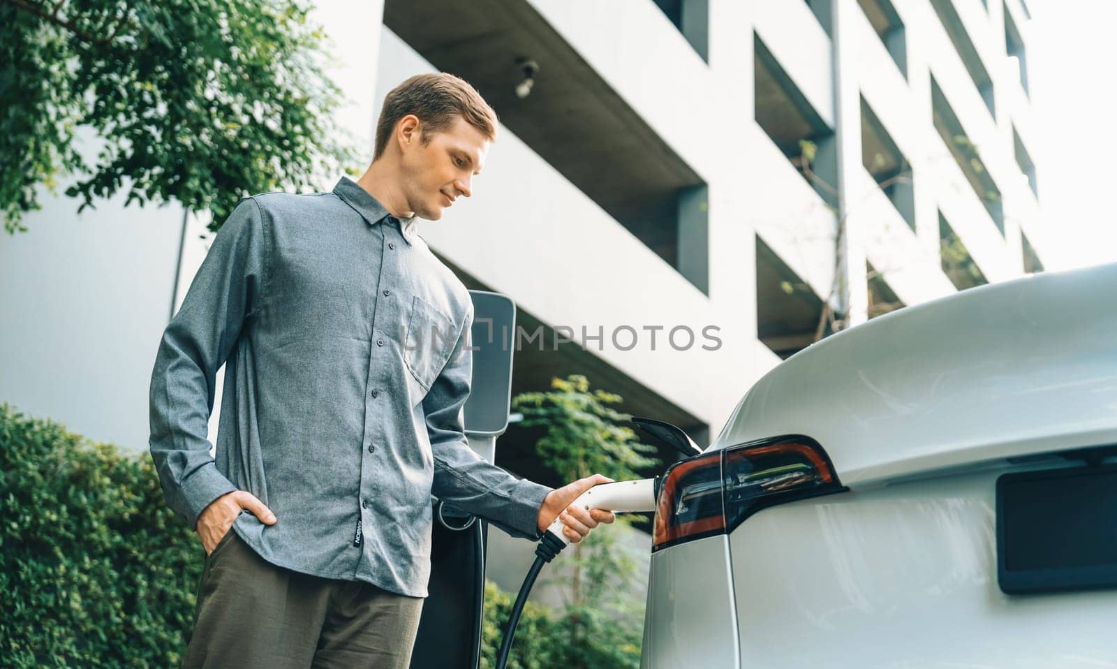 Young man travel with EV electric car in green sustainable city innards by biancoblue