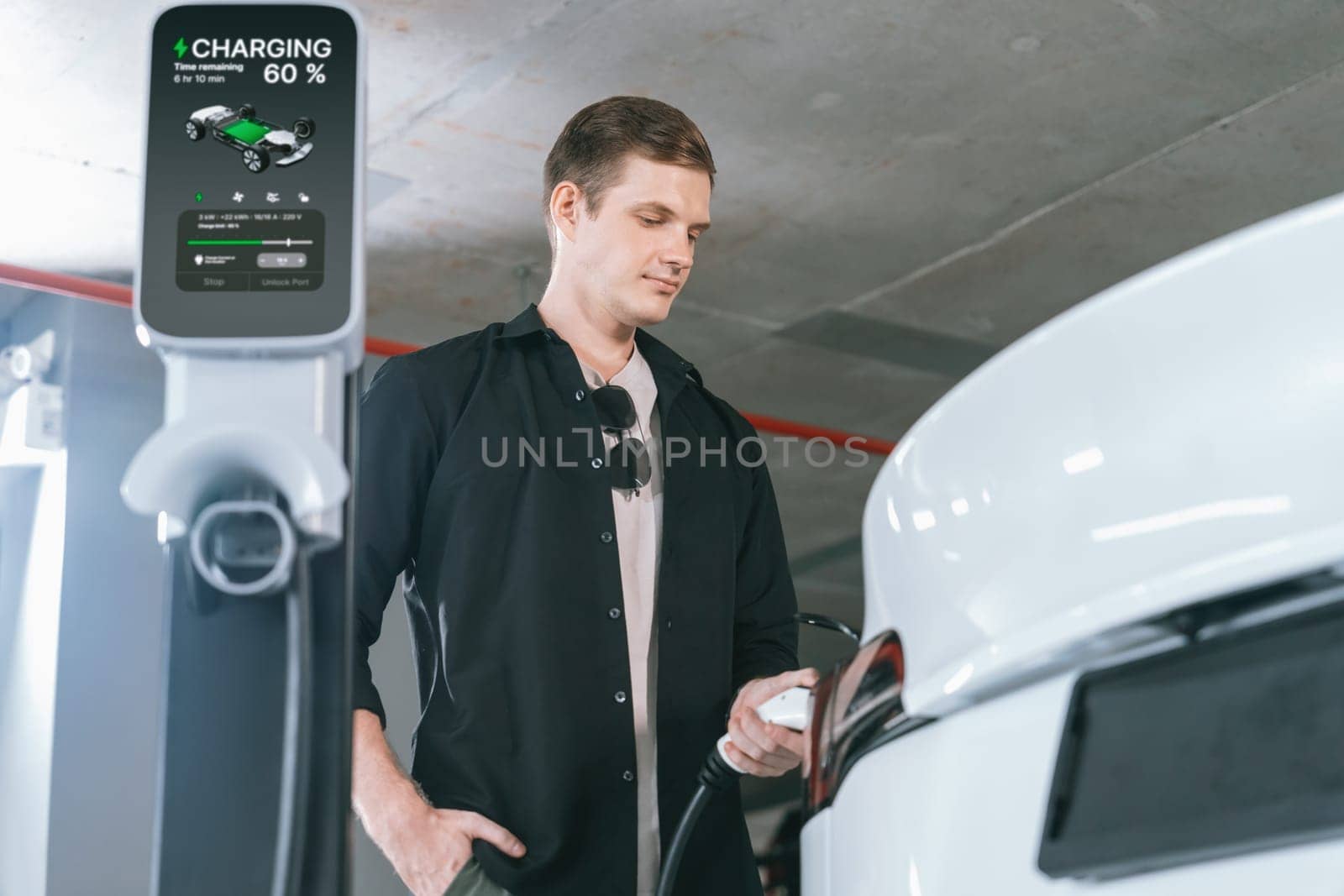 Young man travel with EV electric car to shopping center parking lot charging in downtown city showing urban sustainability lifestyle by green clean rechargeable energy of electric vehicle innards