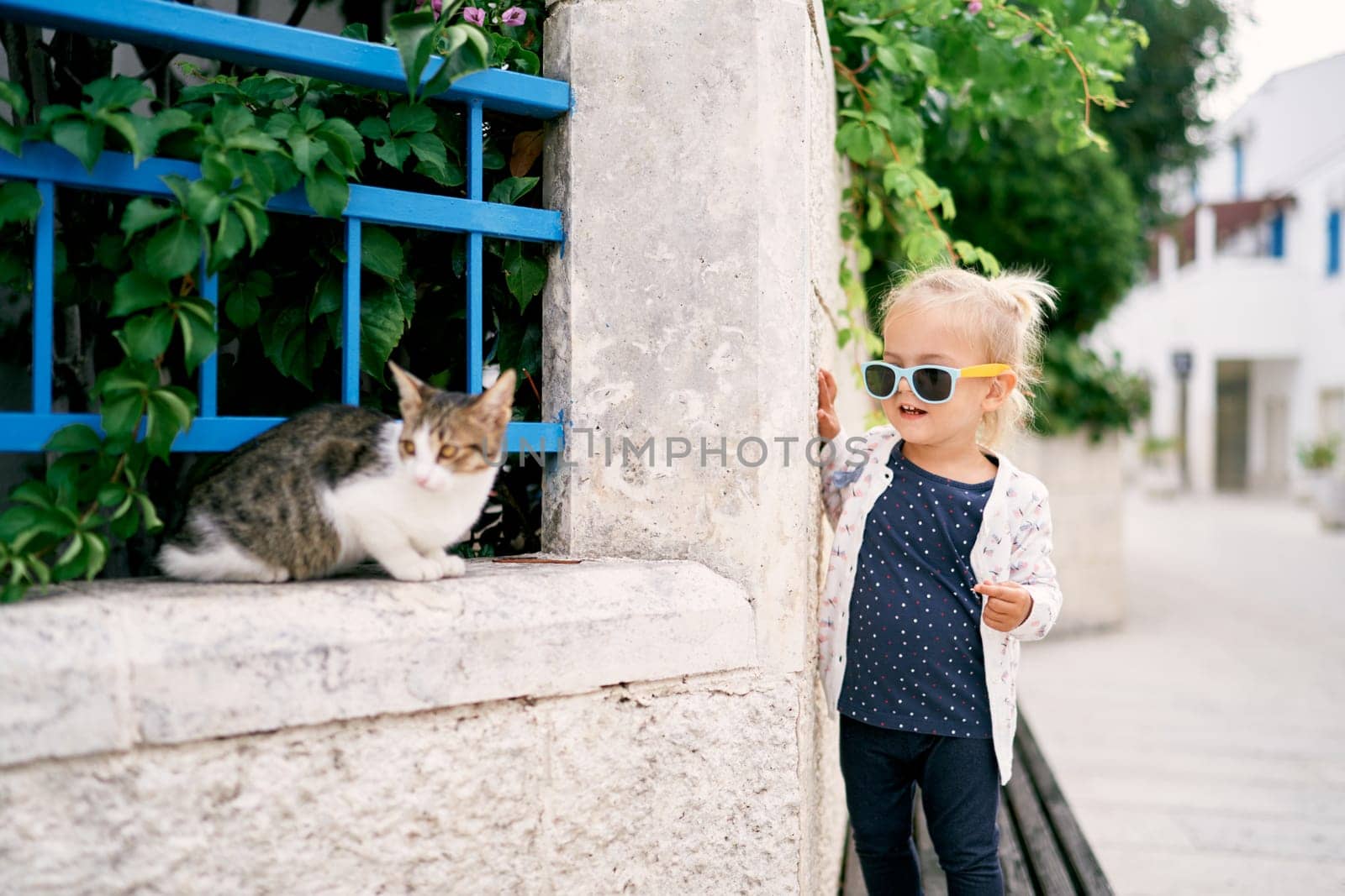Little girl stands on a bench near the fence of the garden and looks out for a cat. High quality photo