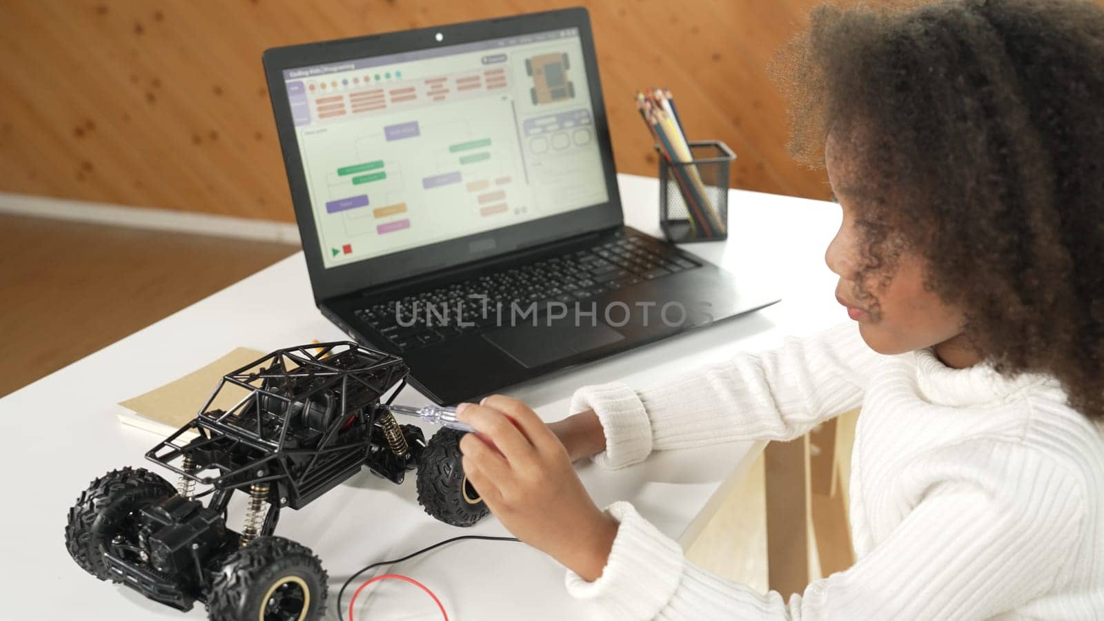 Smart african girl build robotic car while using wires while using laptop setting or writing prompt code. Skilled female student working on computer in STEM technology online classroom. Erudition.