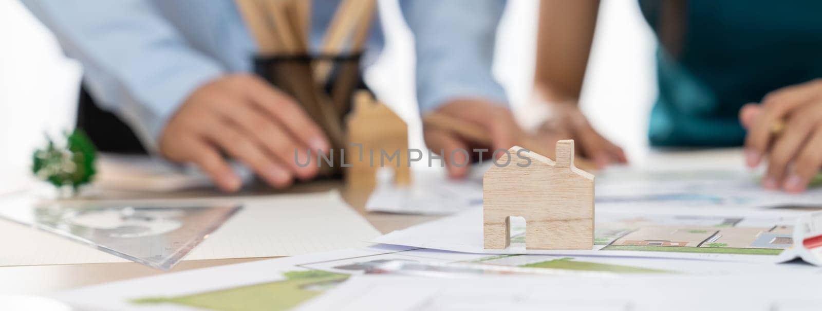 A portrait of professional architect team discussion about architectural project on meeting table with blueprint and wooden block scatter around at modern office. Closeup. Focus hand. Delineation.