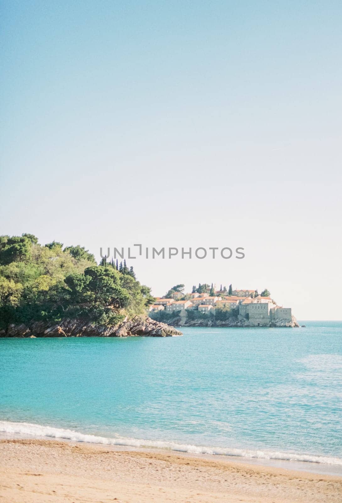 View from the sandy beach of the island of Sveti Stefan, looking out from behind a wooded cliff. Montenegro. High quality photo