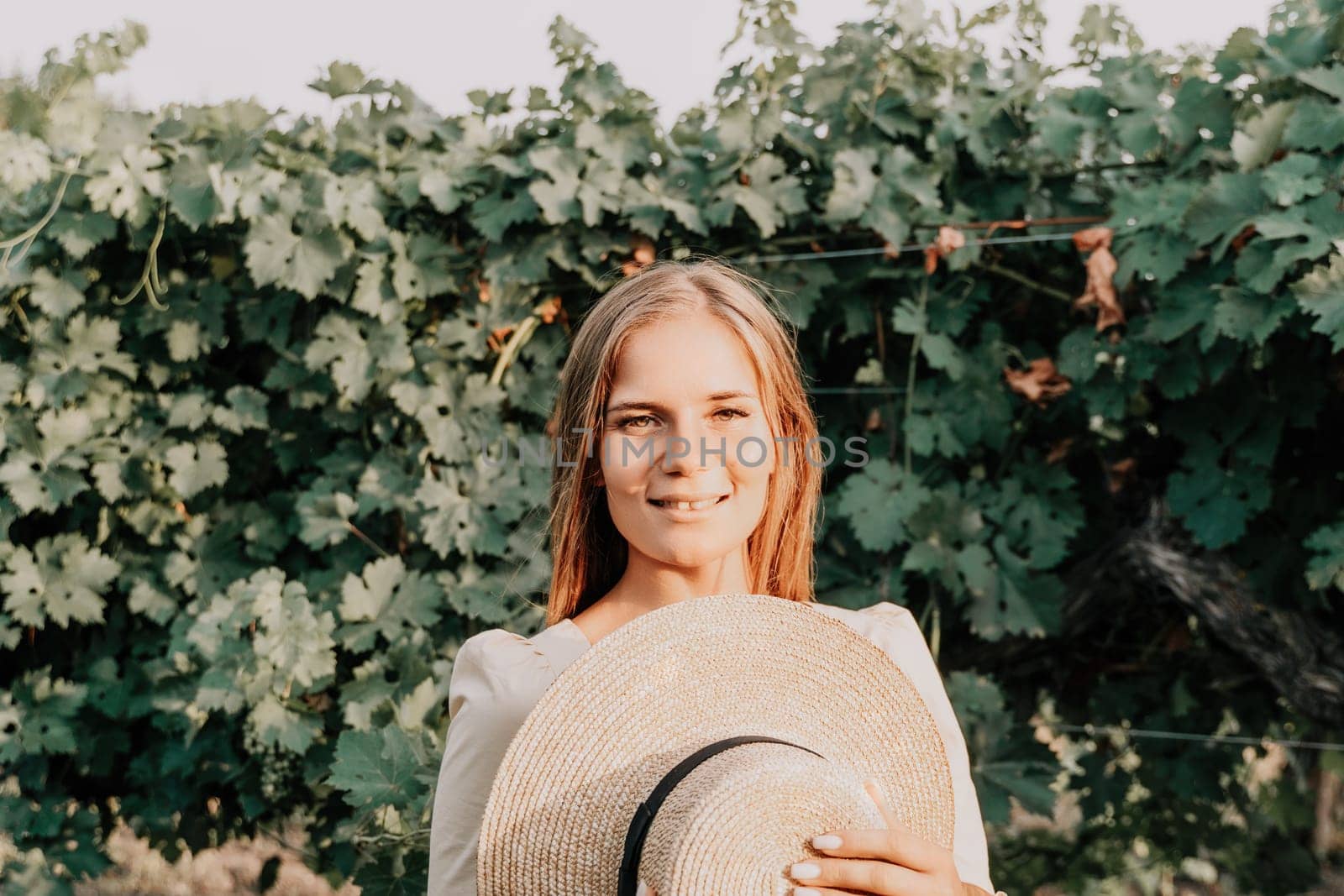 Woman at autumn winery. Portrait of happy woman holding glass of wine and enjoying in vineyard. Elegant young lady in hat toasting with wineglass smiling cheerfully enjoying her stay at vineyard