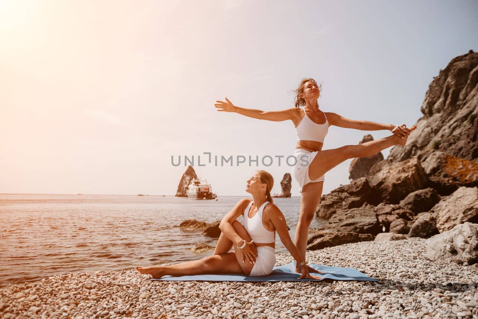 Woman sea yoga. Two happy women practicing yoga on the beach with ocean and rock mountains. Motivation and inspirational fit and exercising. Healthy lifestyle outdoors in nature, fitness concept. by panophotograph