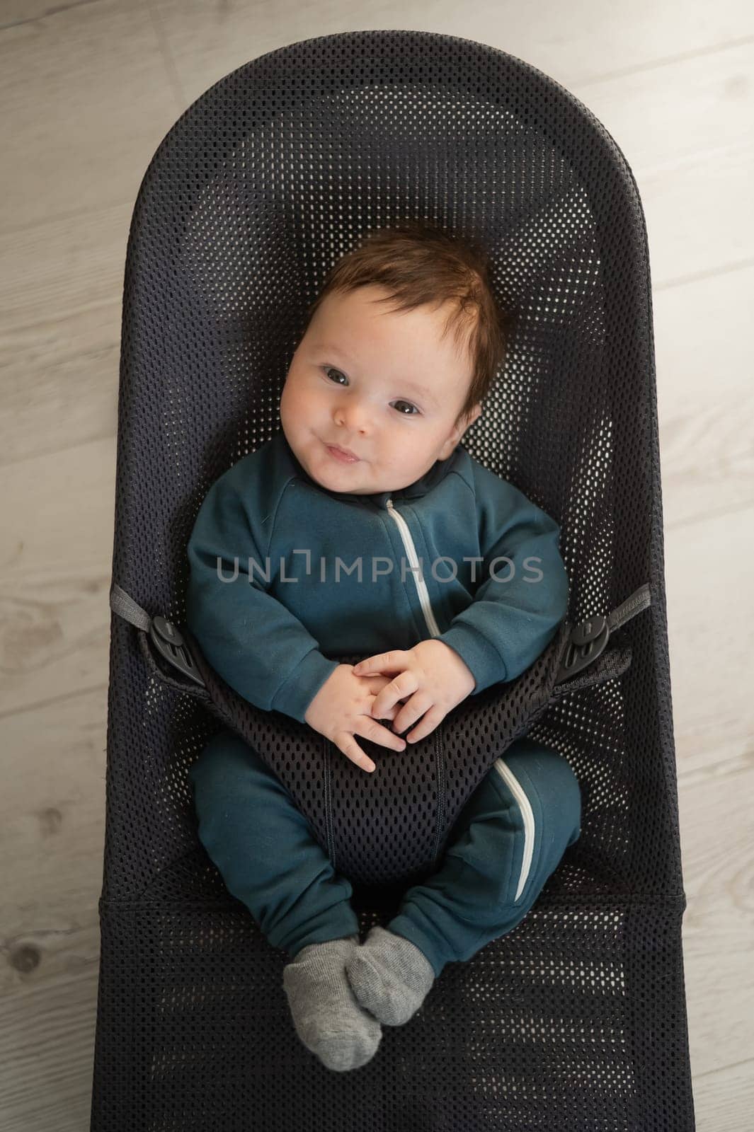 Cute newborn baby dressed in blue overalls sitting in a baby lounger. Vertical photo