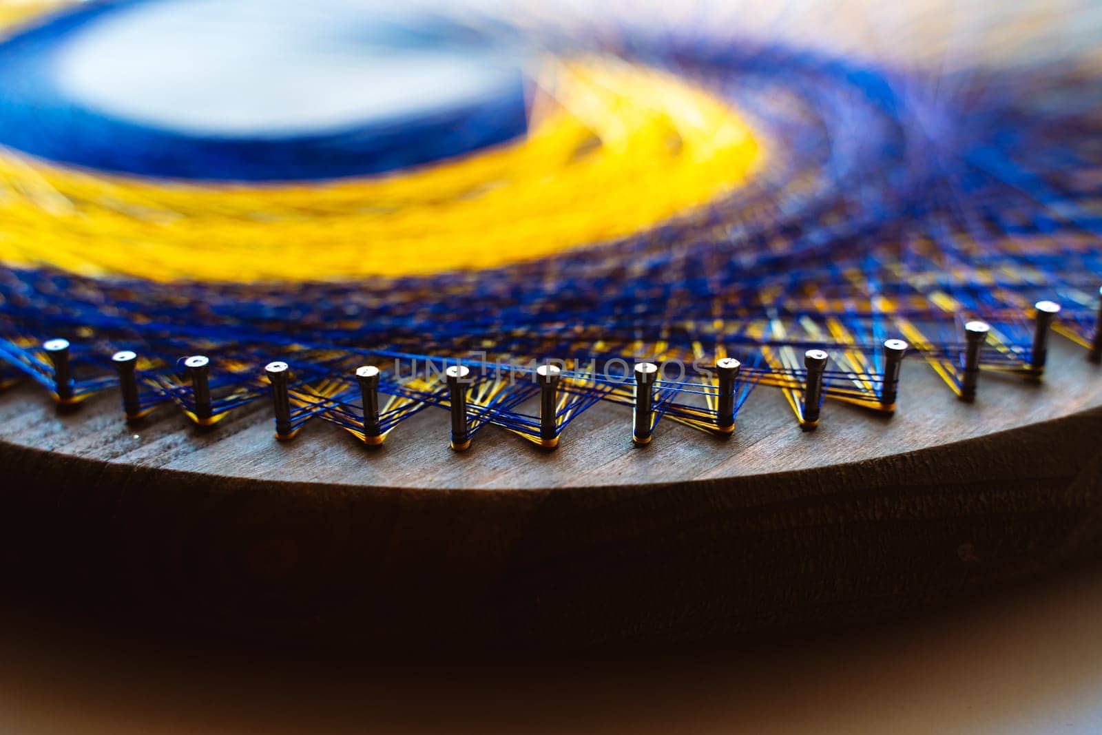 Colored thread mandala on a wooden board with nails. Mandala Moon Harmony Sun esotericism and psychology pictures from yellow and blue silk threads. by Matiunina