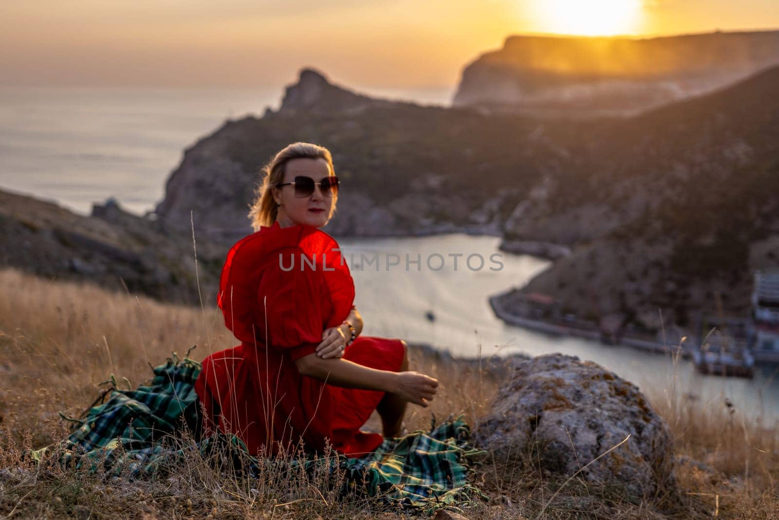 Woman sunset sea mountains. Happy woman siting with her back on the sunset in nature in summer posing with mountains on sunset, silhouette. Woman in the mountains red dress, eco friendly, summer landscape active rest by Matiunina