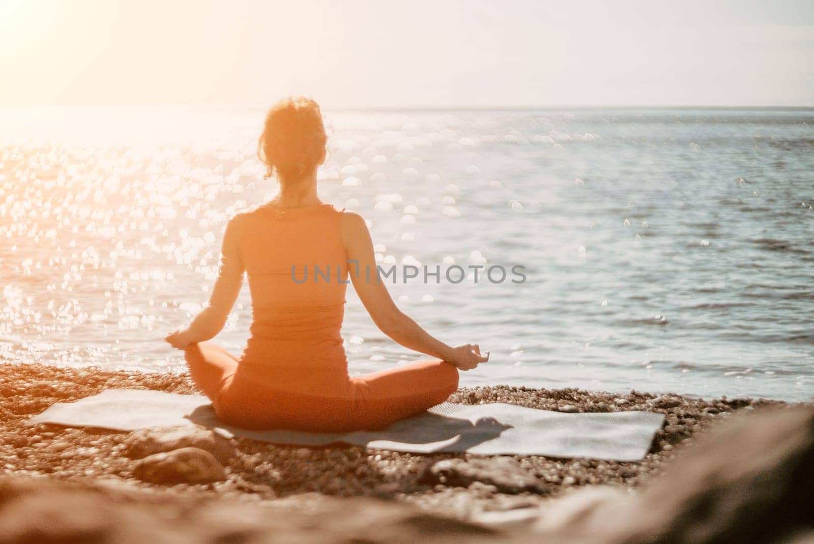 Woman sea yoga. Selective focus. Young beautiful caucasian woman in a red suit practicing yoga on the beach at sunrise near the sea. Yoga. Healthy lifestyle. Meditation concept. by panophotograph