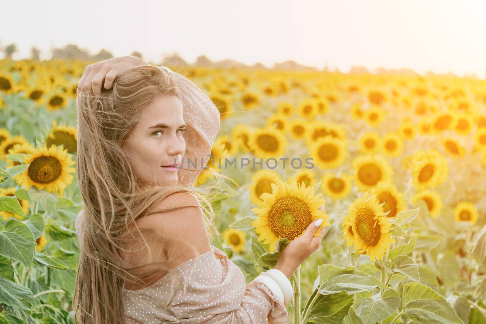 Woman in Sunflower Field: Happy girl in a straw hat stands in a vast field of sunflowers at sunset. Summer time. by panophotograph