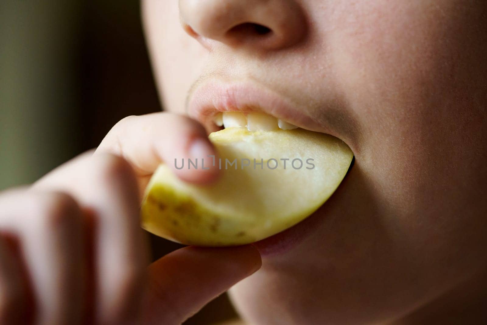 Closeup of crop unrecognizable young girl biting fresh juicy apple piece at home