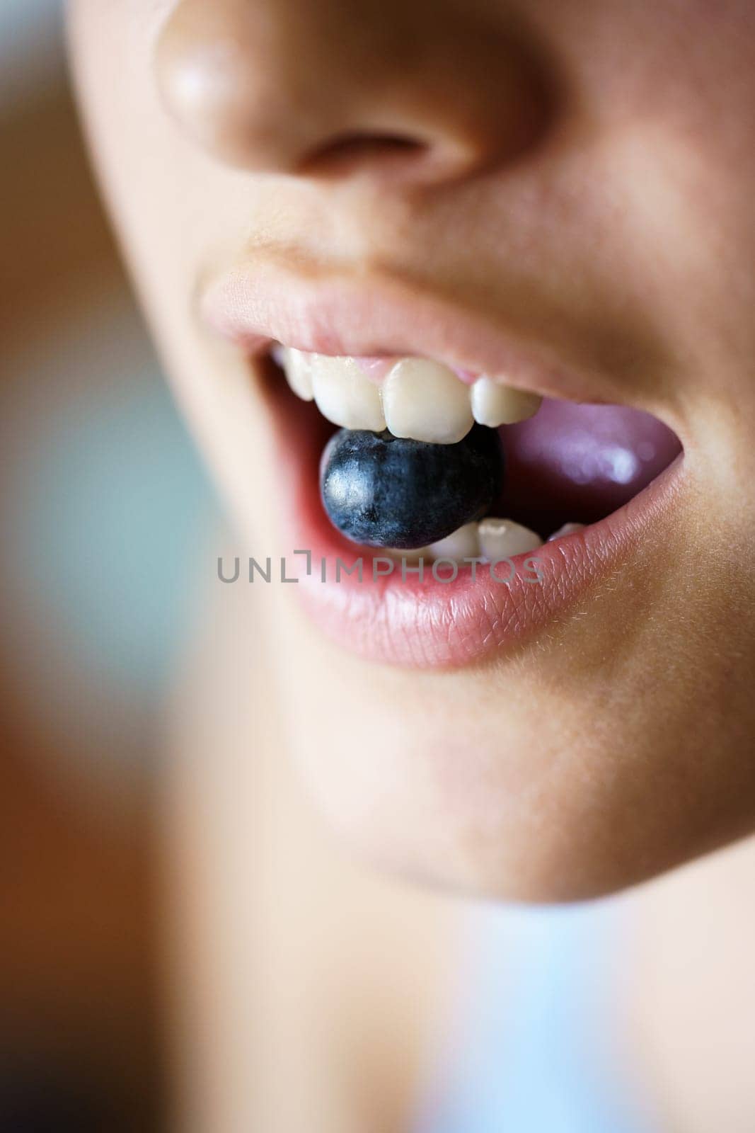 High angle closeup of unrecognizable crop young girl holding fresh blueberry between teeth at home
