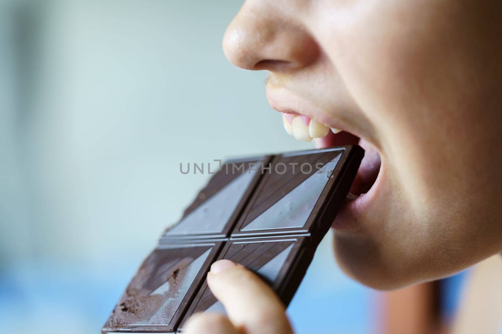 Anonymous girl with mouth open eating chocolate bar at home by javiindy