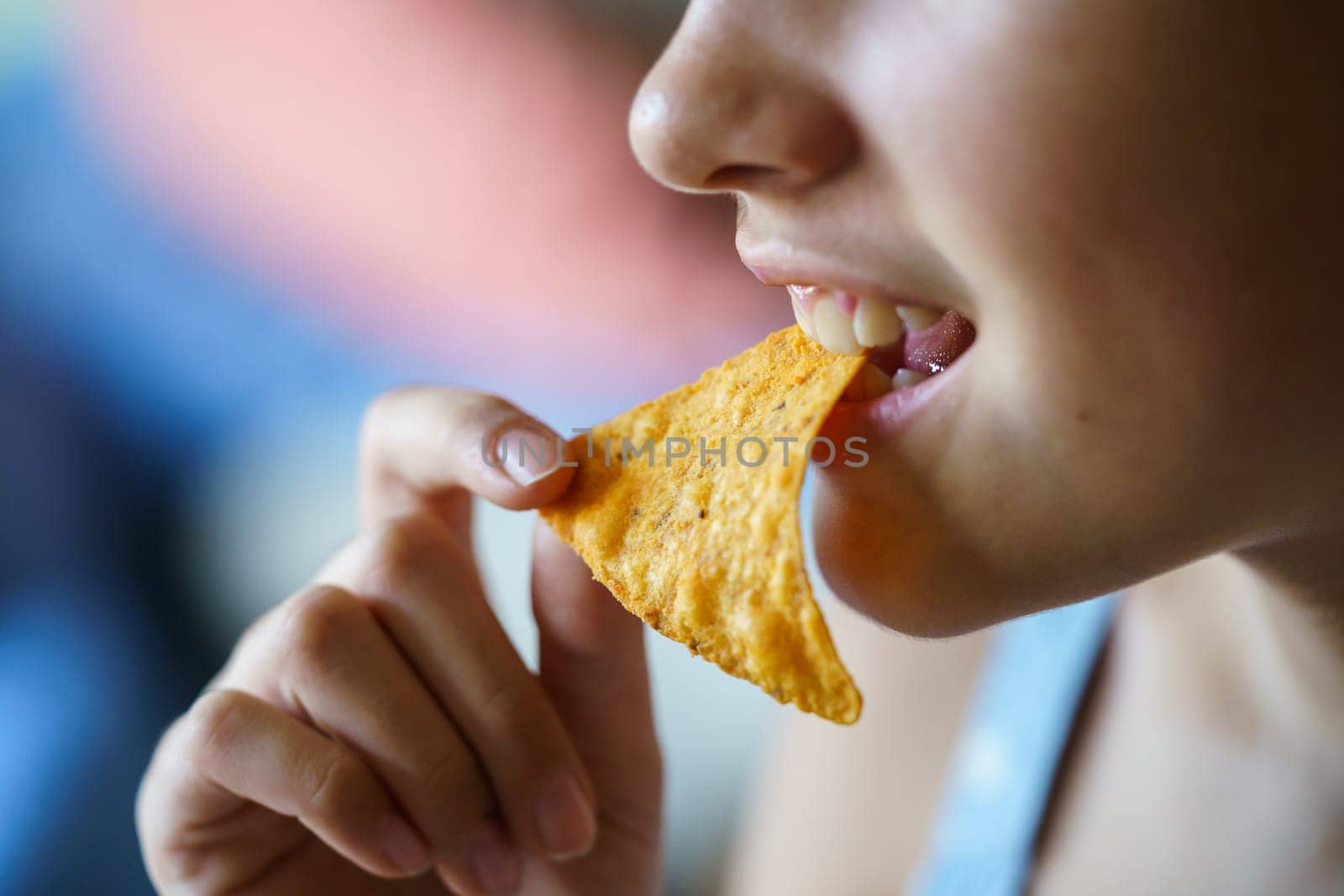 Closeup of crop unrecognizable happy teenage girl biting spicy nacho chip at home