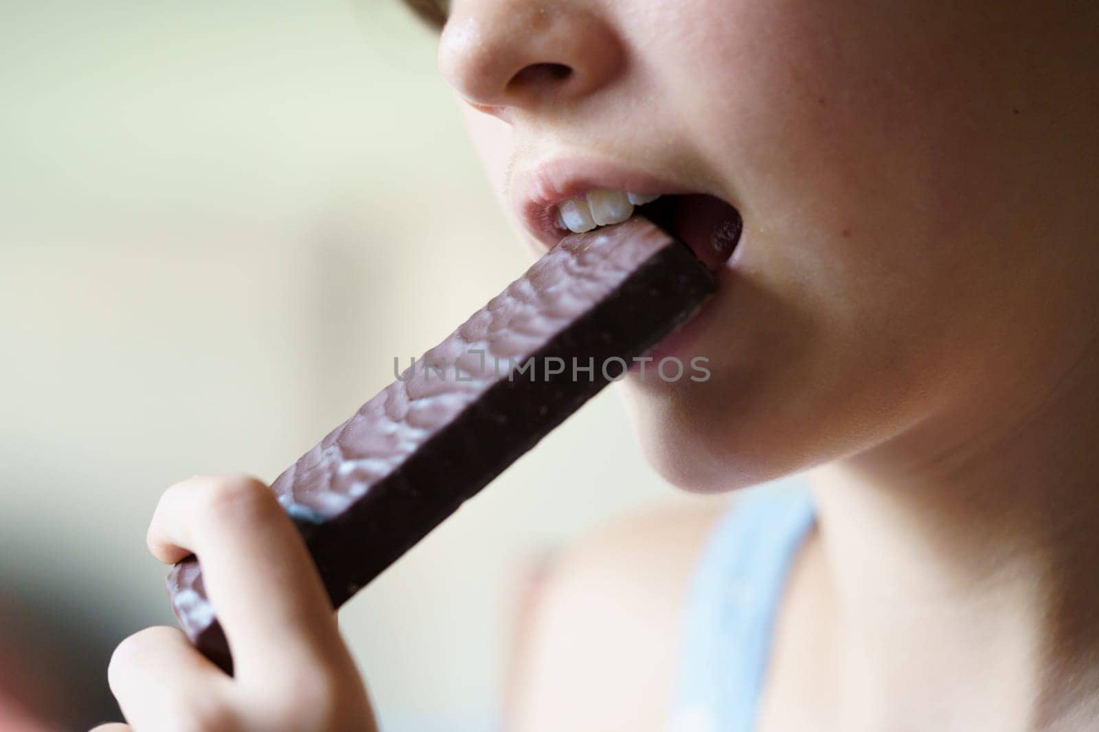 Closeup of crop unrecognizable teenage girl eating healthy protein bar at home