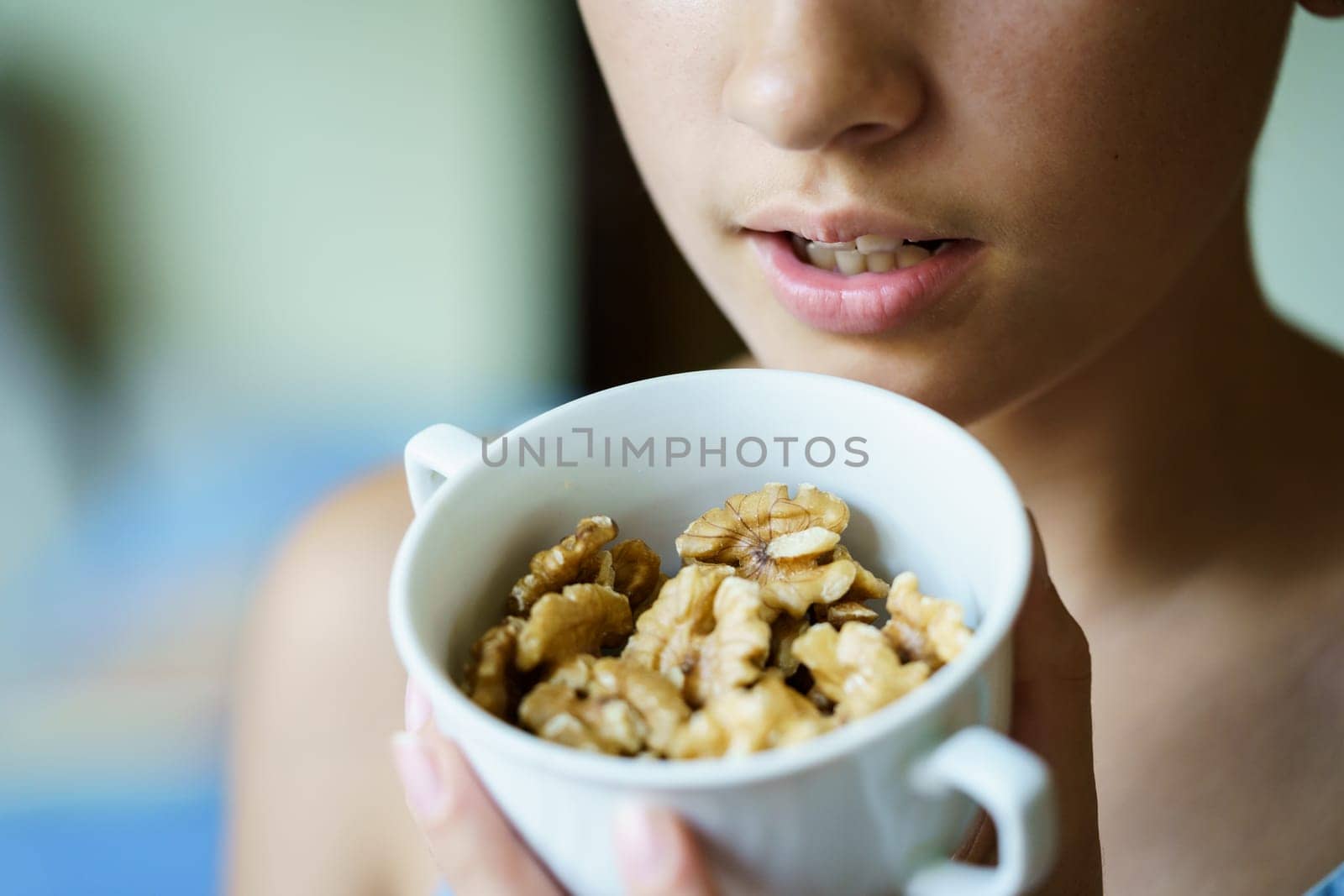 Closeup of crop unrecognizable teenage girl holding fresh walnuts in cup at home