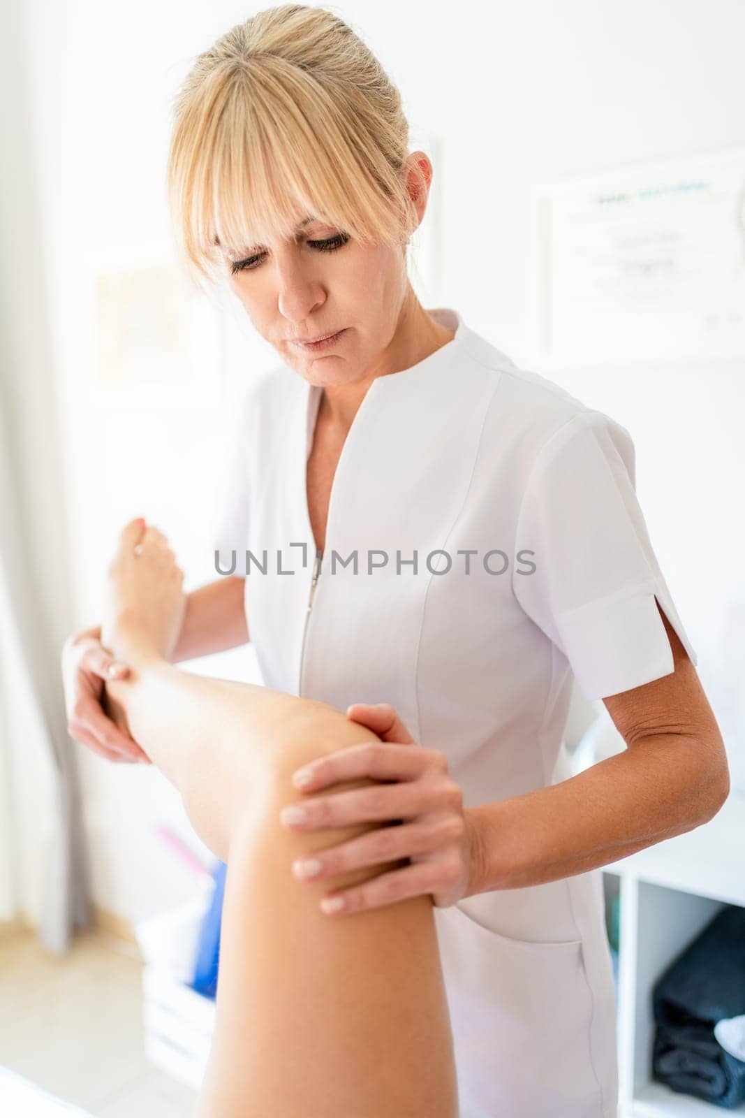 Professional physiotherapist doing rehabilitation massage on leg of female patient during appointment in modern clinic center