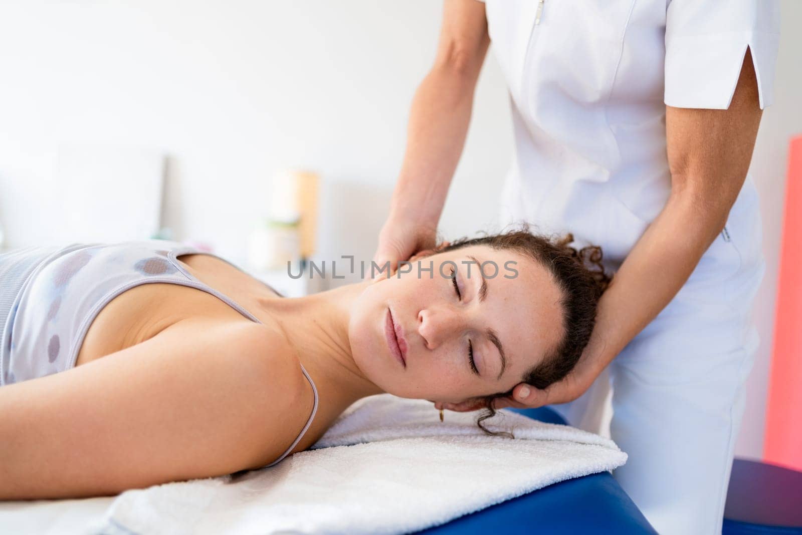 Crop anonymous female manual therapist massaging neck of young woman lying on couch during rehabilitation session