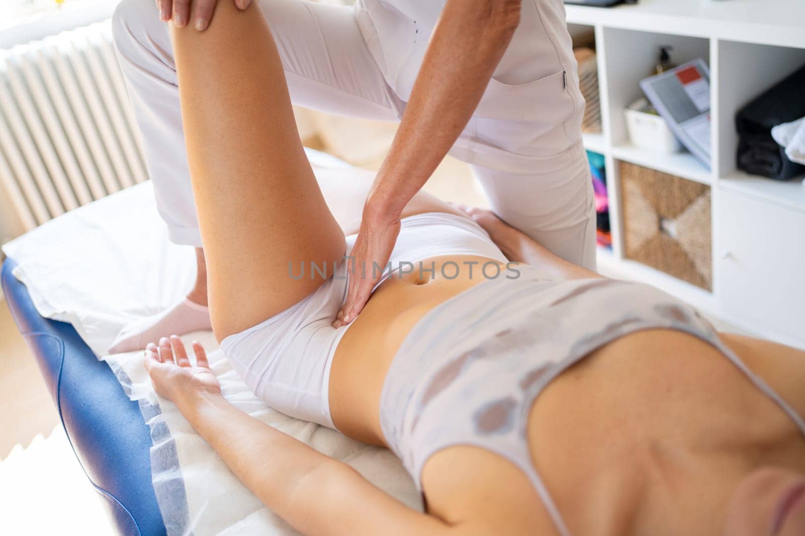 High angle of crop anonymous female physical therapist rubbing belly of patient lying with raised leg during physiotherapy session