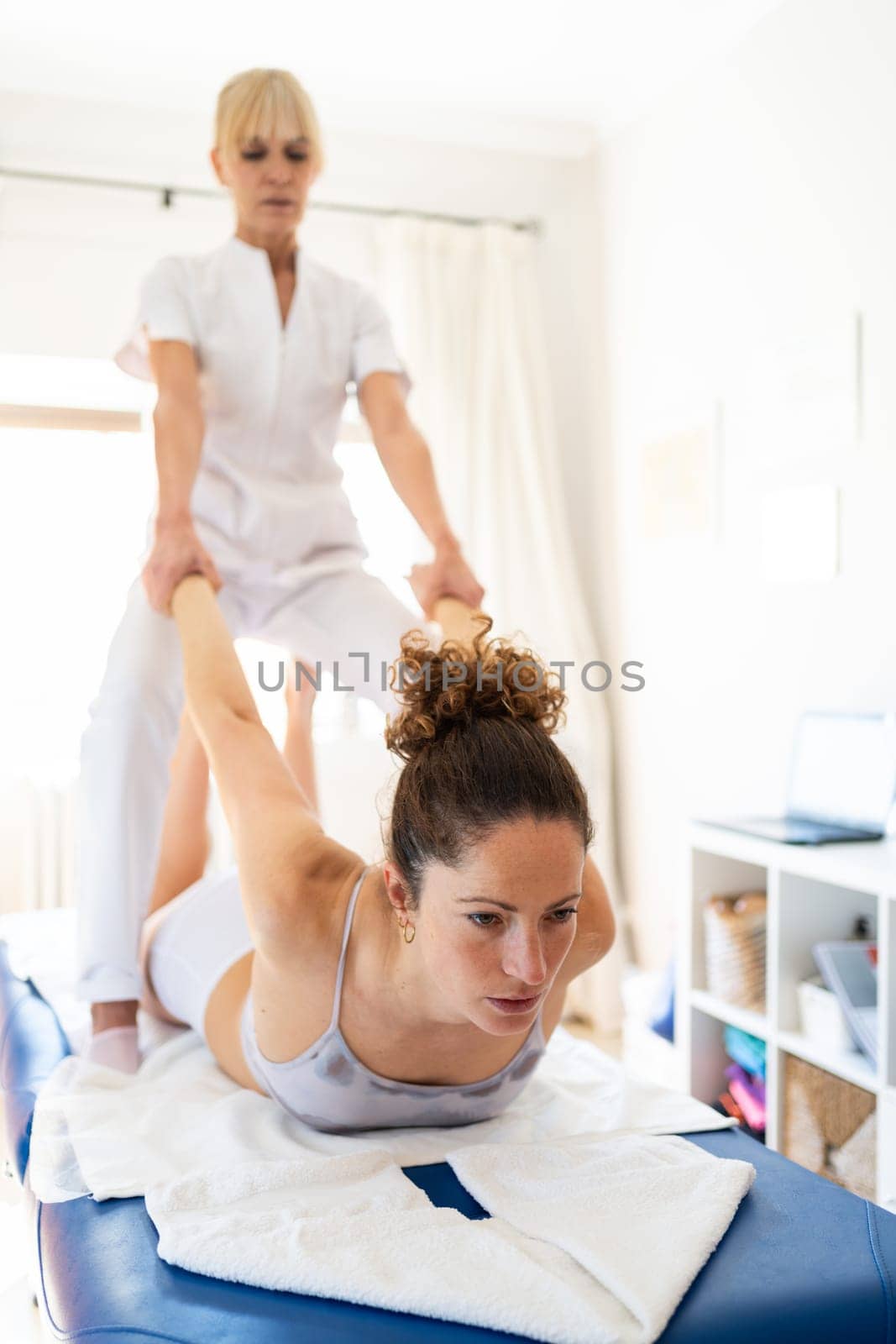 Professional manual therapist pulling hands of woman lying on belly fixing back and shoulder joint during psychotherapy session